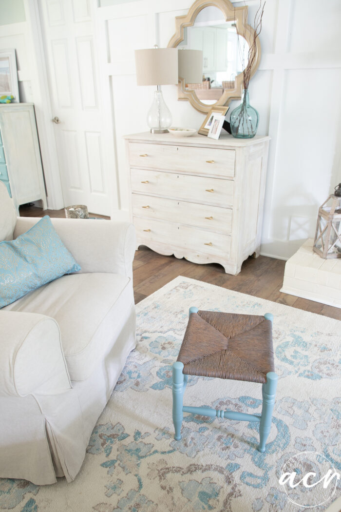 coastal style home with white walls blue footstool and gold mirror