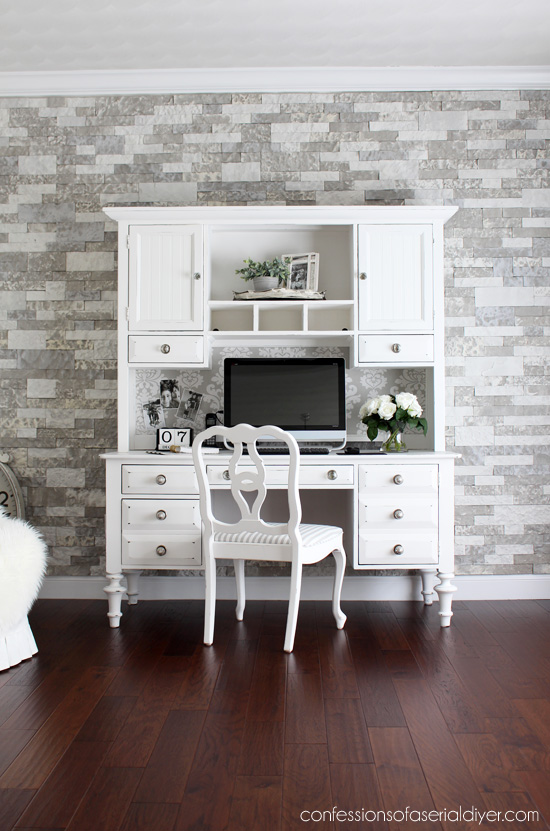 dark wood floor with white desk and chair and multi gray colored brick/stone wall
