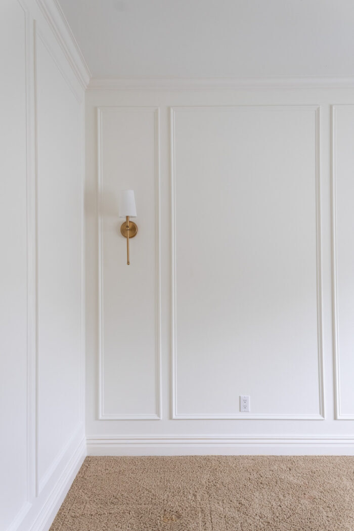 white wall with simple wainscoting and gold lamp