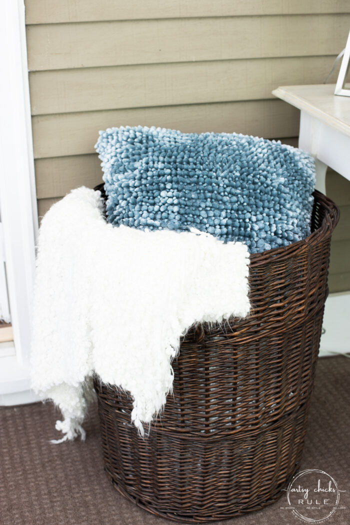 dark brown tall stained basket with white throw and blue pillow